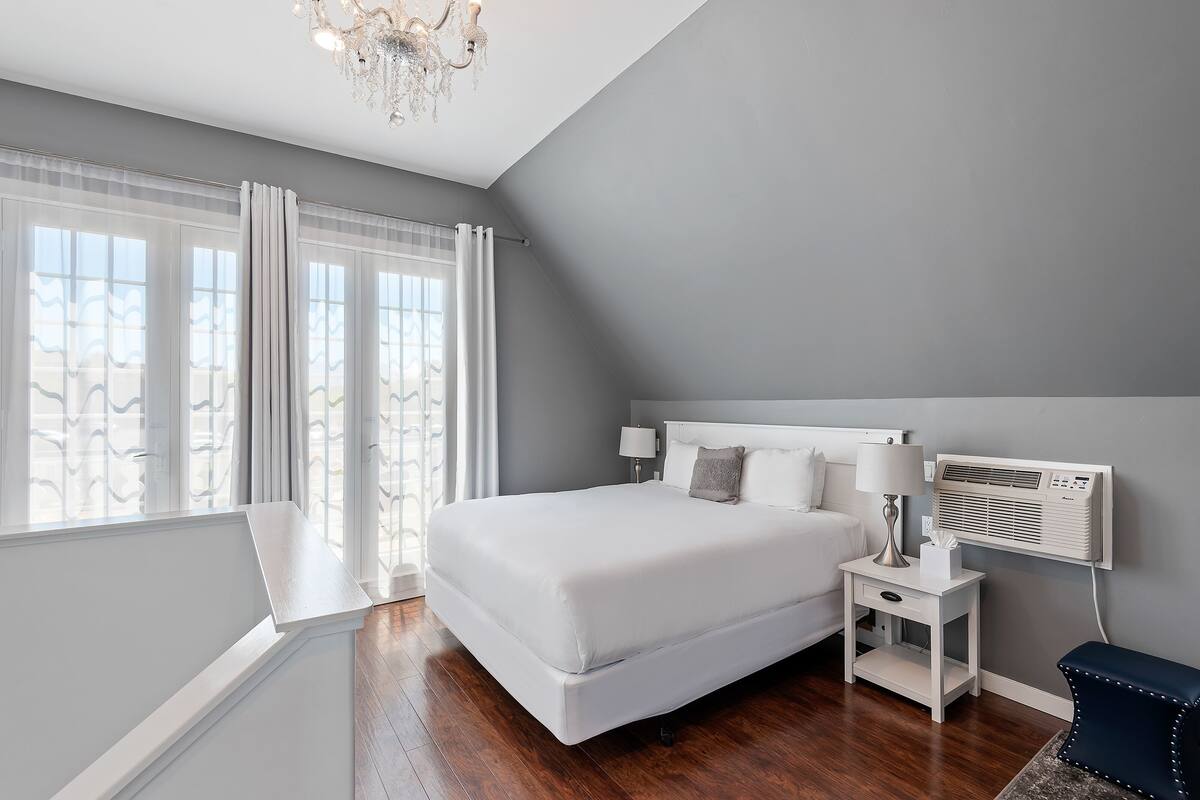 Ein Schlafzimmer mit einem großen Bett, einem Nachttisch mit Lampe, einer Wand-Klimaanlage und Blick ins Freie durch große Fenster.