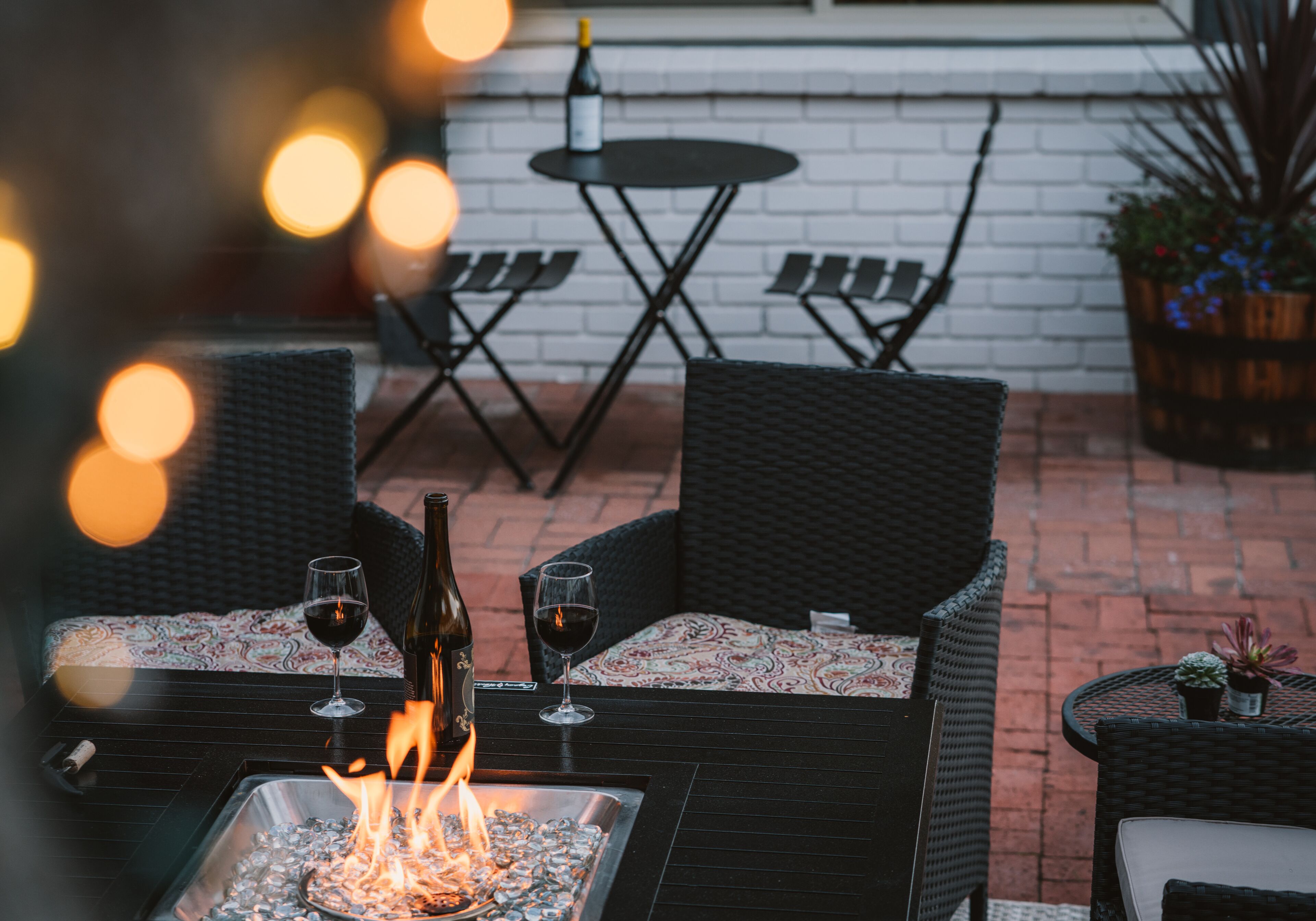 An outdoor patio with wicker furniture, a fire feature, and a bottle of wine.