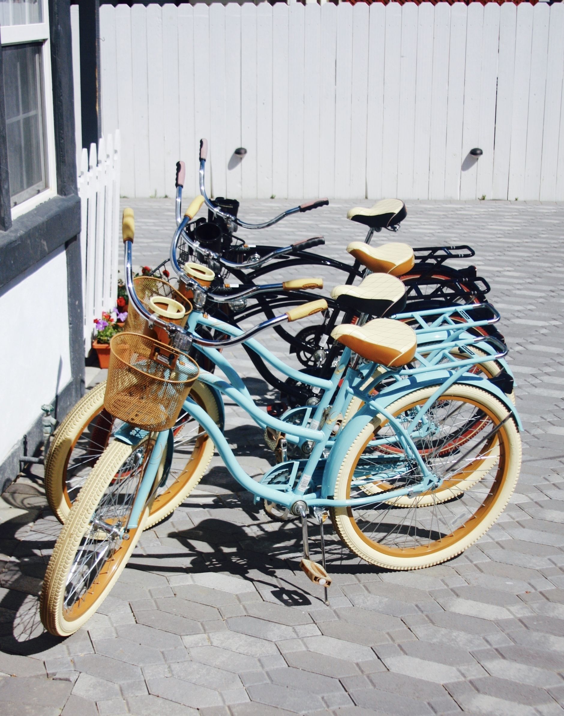 A row of bicycles parked against a white fence.