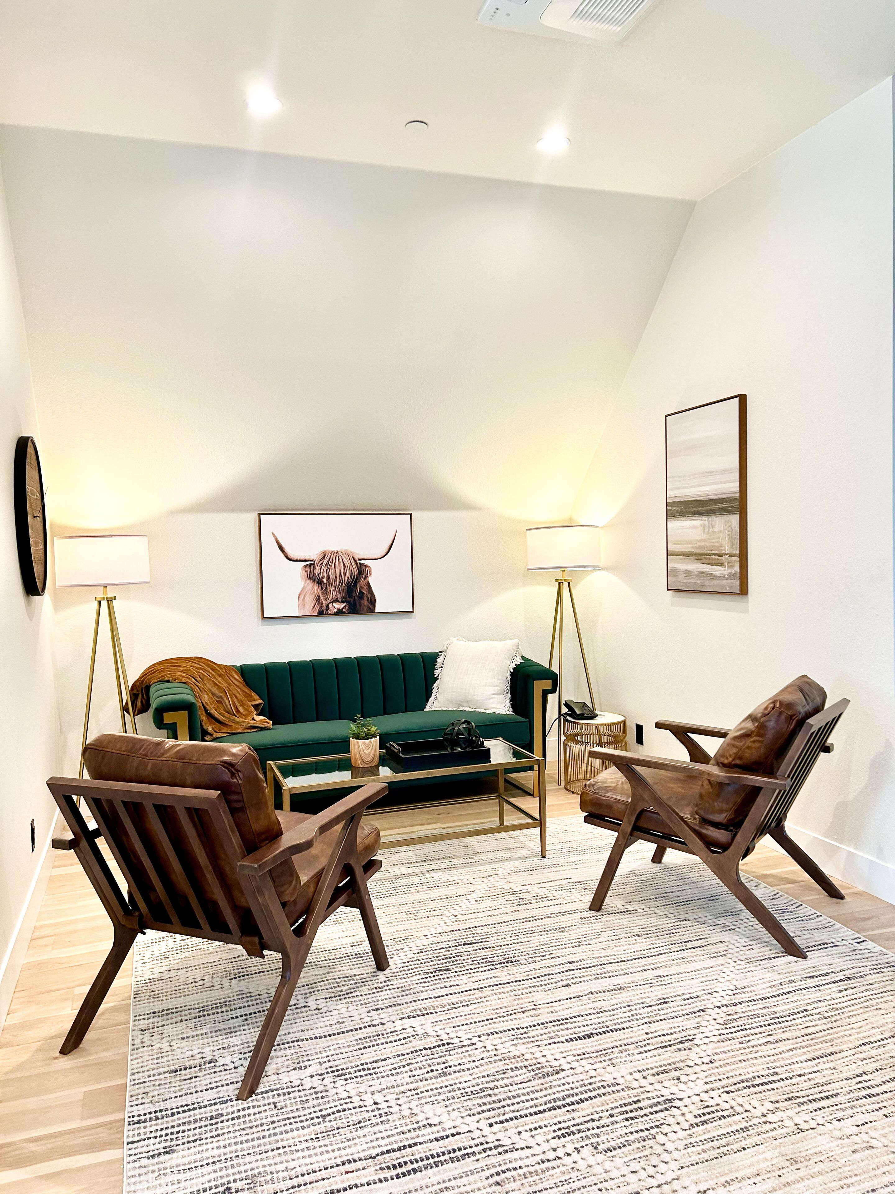 A modern living room with a green sofa, two leather armchairs, a coffee table, and a patterned rug.