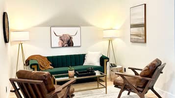 A modern living room with a green sofa, two leather armchairs, a coffee table, and a patterned rug.