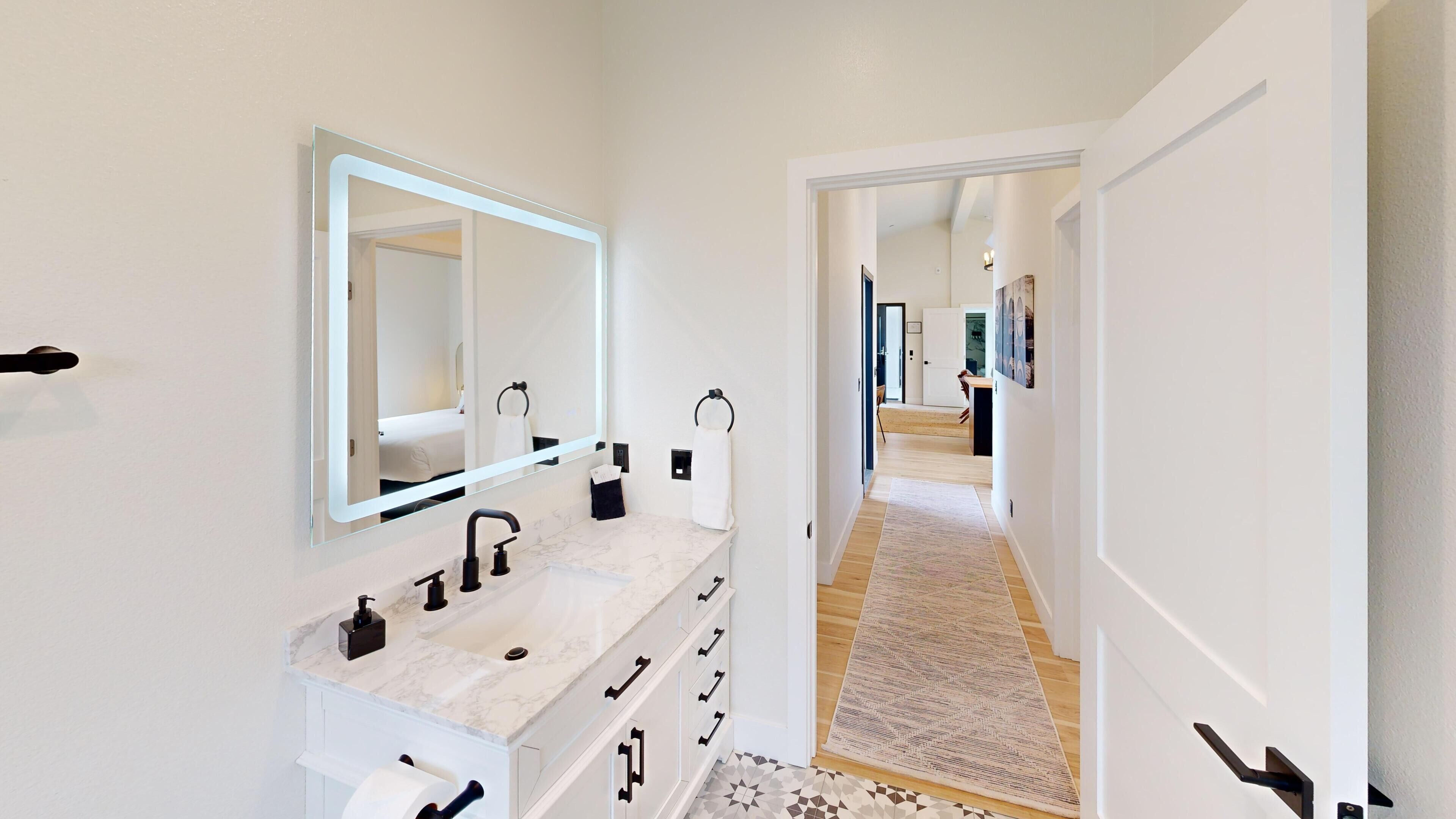 A modern bathroom with a marble sink, a large mirror, and a walk-in shower.