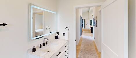 A modern bathroom with a marble sink, a large mirror, and a walk-in shower.