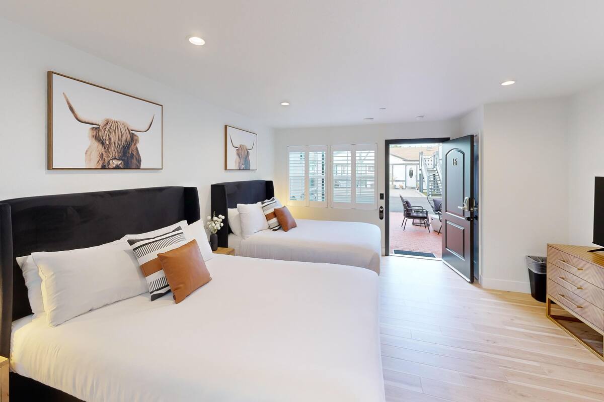 Ein Hotelzimmer mit zwei Betten, einem Fernseher, einer Holzkommode und einem Balkon mit Blick auf die Straße.