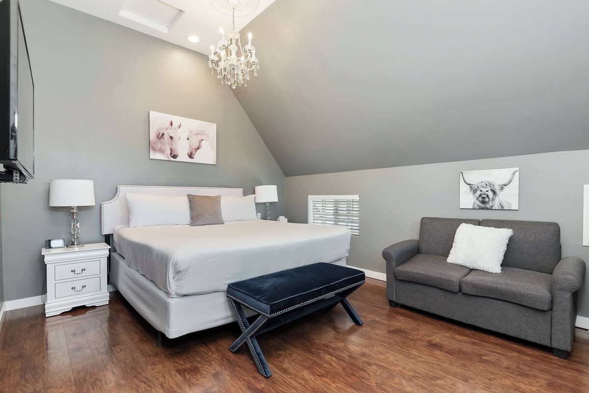 Ein Schlafzimmer mit einem Bett, Nachttischen, einer Bank, einer Couch und Kunstwerken an den Wänden.