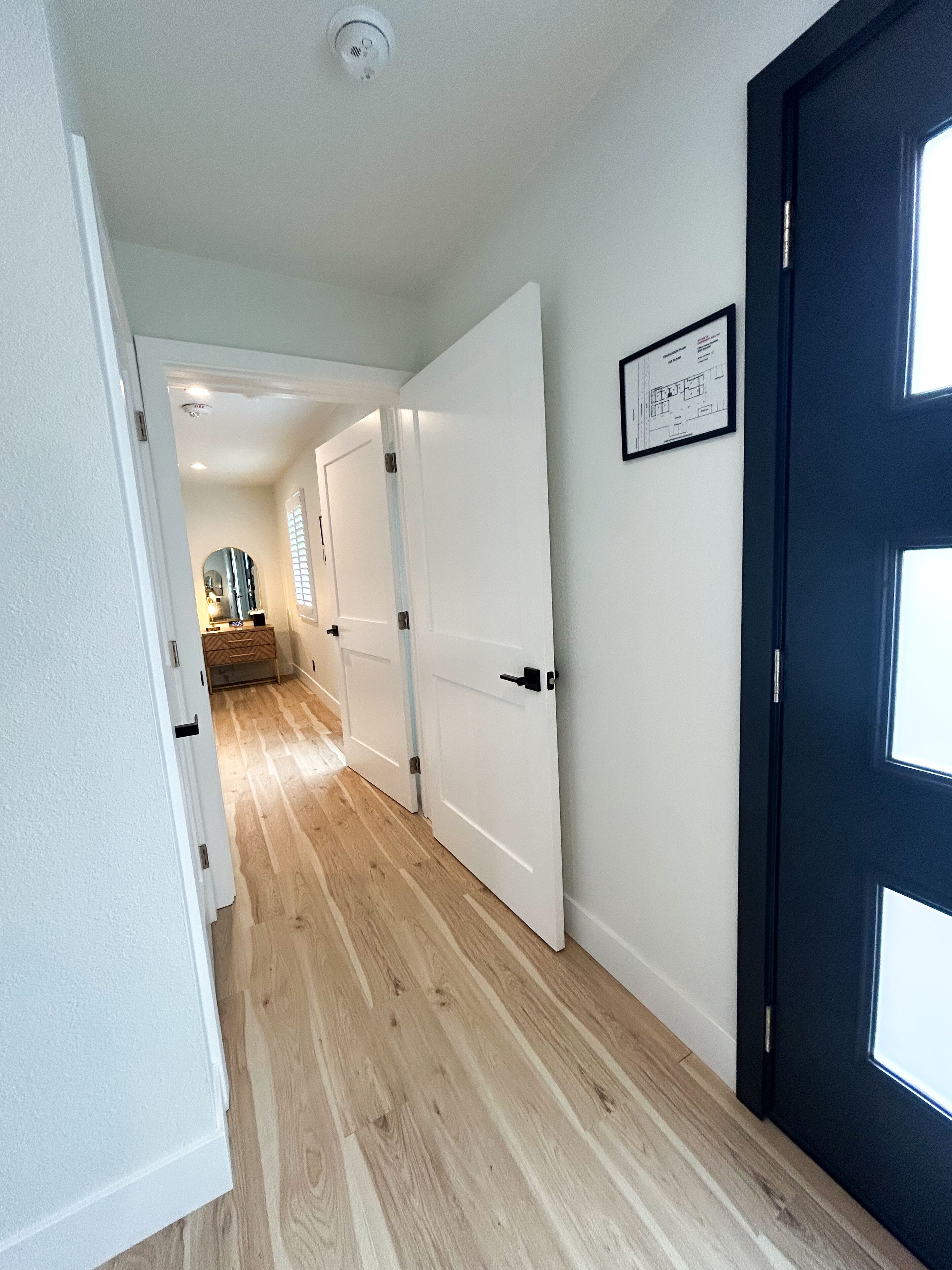 A hallway with wooden flooring, white walls, and a black door.