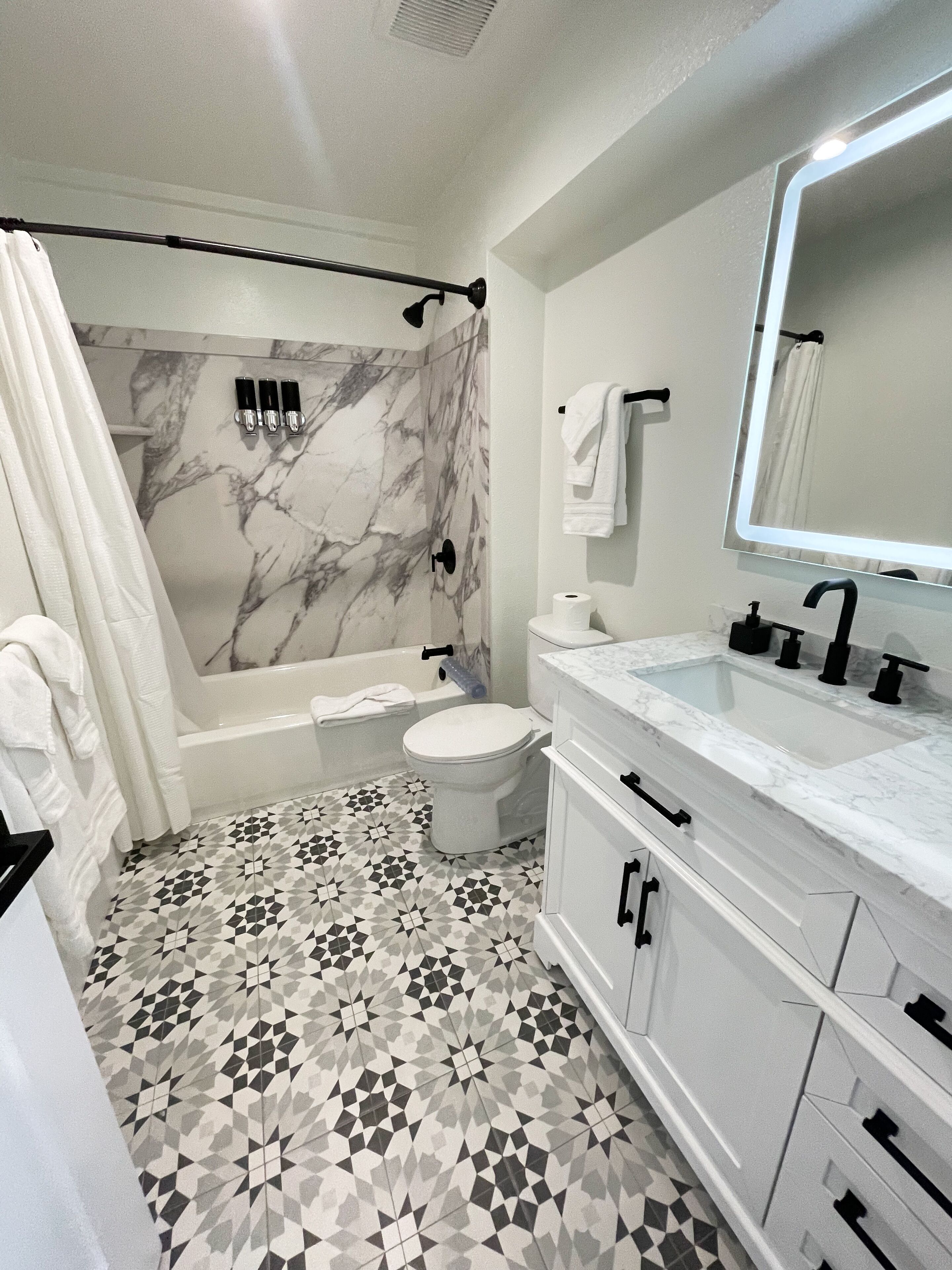 Un baño moderno con pared de ducha de mármol, una bañera independiente, un inodoro y un lavamanos con un espejo grande.
