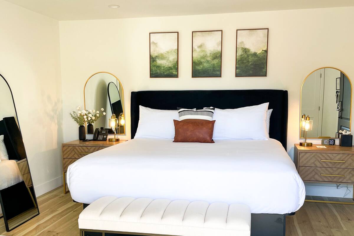 Ein modernes Schlafzimmer mit einem großen Bett, Nachttischen, einem Spiegel und Kunstwerken an der Wand.