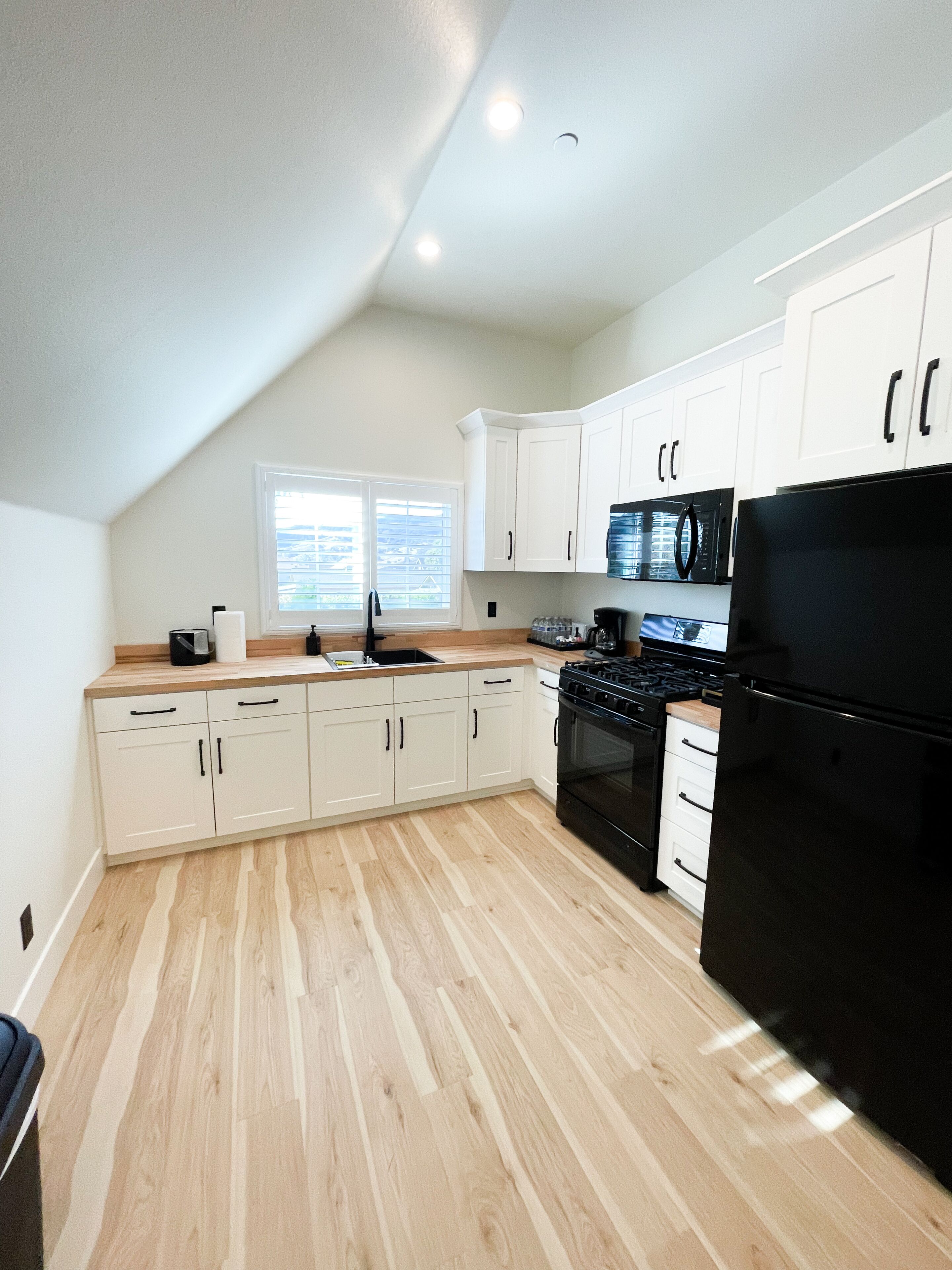 A modern kitchen with white cabinets, a black refrigerator, and a wooden floor.