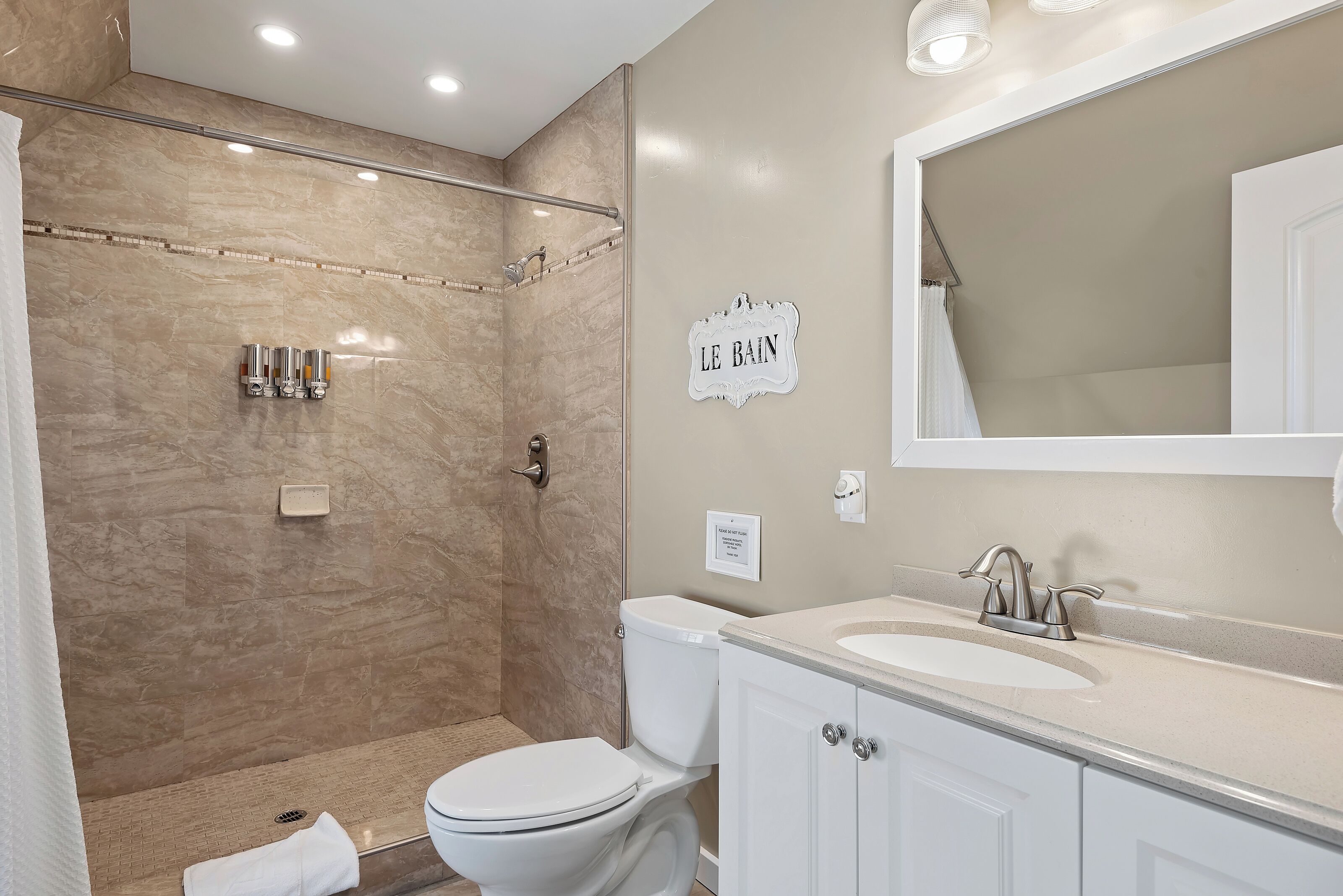A bathroom with a shower, toilet, sink, and a sign that reads "LE BAIN".
