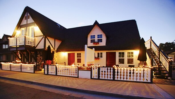 A traditional building with a balcony, a staircase, and a fence with lights. - New Haven Inn (Solvang)