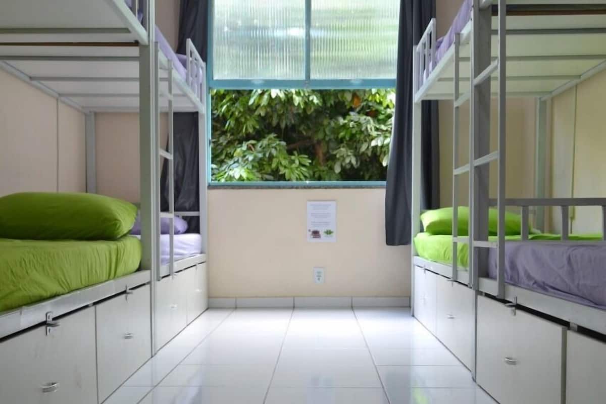 A dormitory room with bunk beds, a window with curtains, and a tiled floor.