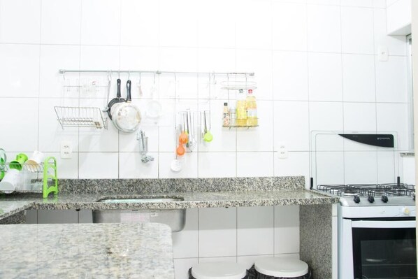 A kitchen with white tiles, a granite countertop, a stove, and a hanging rack with utensils.