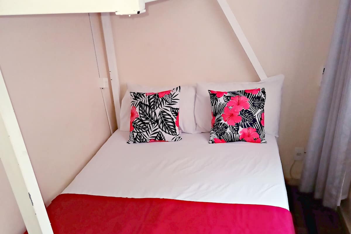 A bunk bed with a white frame, two pillows with a tropical leaf pattern, and a red bedspread.