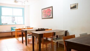 A dining area with multiple tables and chairs, a window with blue trim, and a framed artwork on the wall. - Solar Hostel Beach Copacabana (Rio de Janeiro)