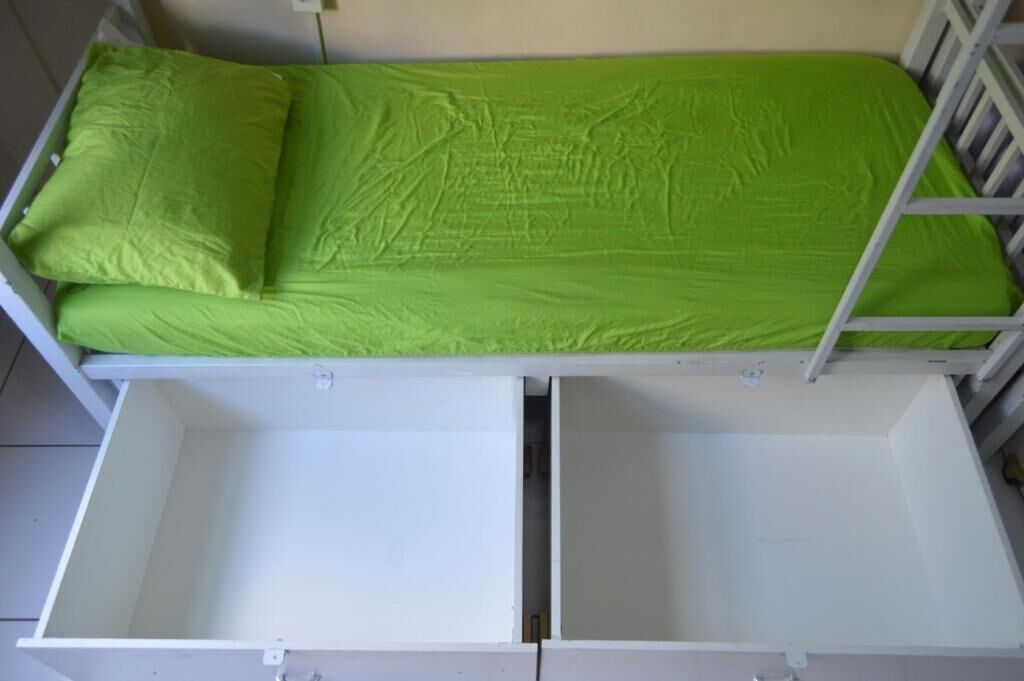 A bunk bed with a green mattress and two white drawers below.