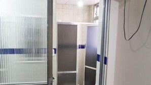 A bathroom with a toilet, a shower, and a glass door leading to another room. - Solar Hostel Beach Copacabana (Rio de Janeiro)