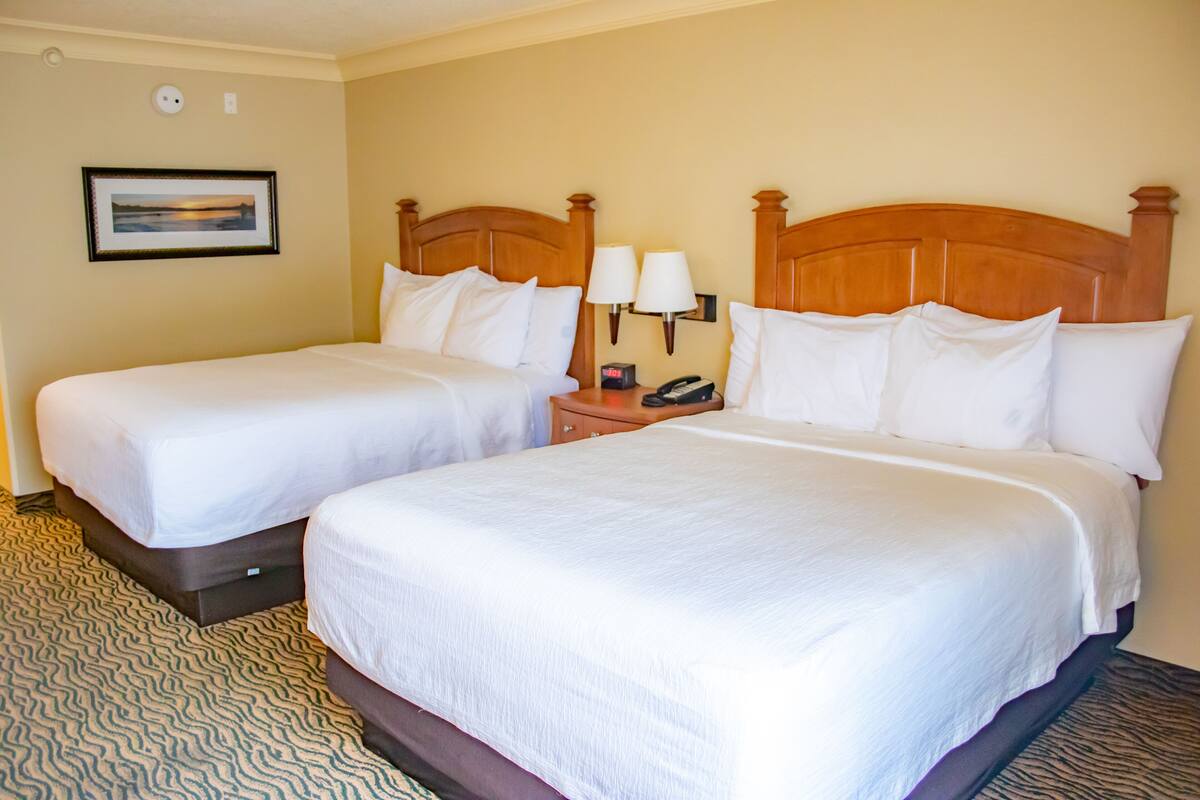 A hotel room with two beds, a nightstand with a lamp, and a framed picture on the wall.