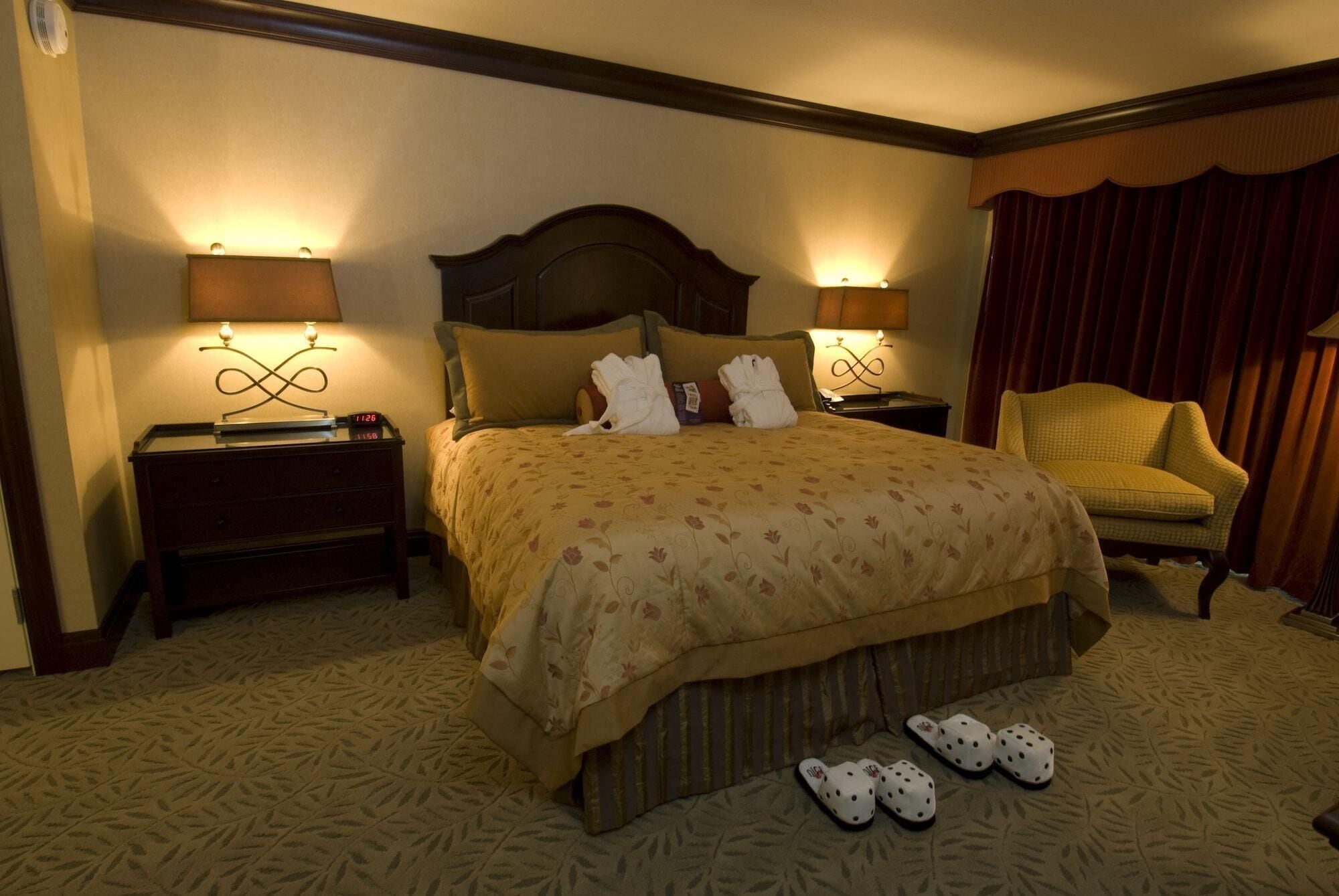 Une chambre d’hôtel avec un grand lit, deux tables de chevet avec des lampes, une chaise et un sol recouvert d’une moquette.