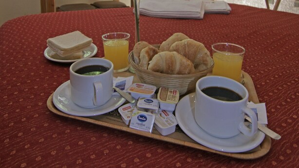 A neatly arranged breakfast tray on a bed with croissants, coffee, juice, and a vase of flowers. - Xumec Apart Hotel (Mendoza)