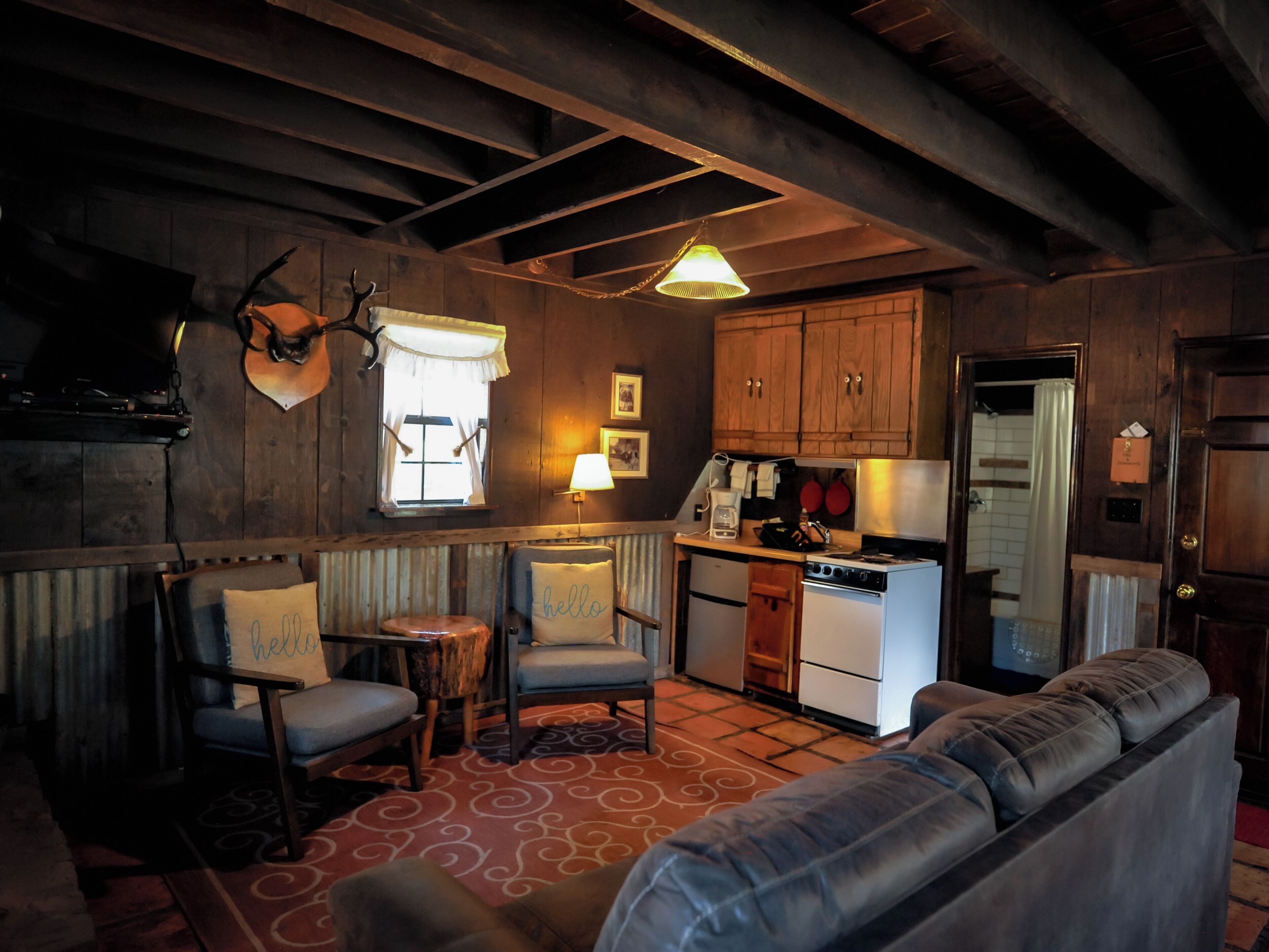 A cozy cabin interior with a wooden ceiling, a dining area with a table and chairs, a kitchenette, and a living room with a sofa.