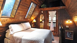 A cozy attic bedroom with a large bed, wooden walls, and a skylight. - Bear Creek Motel And Cabins (Silver City)