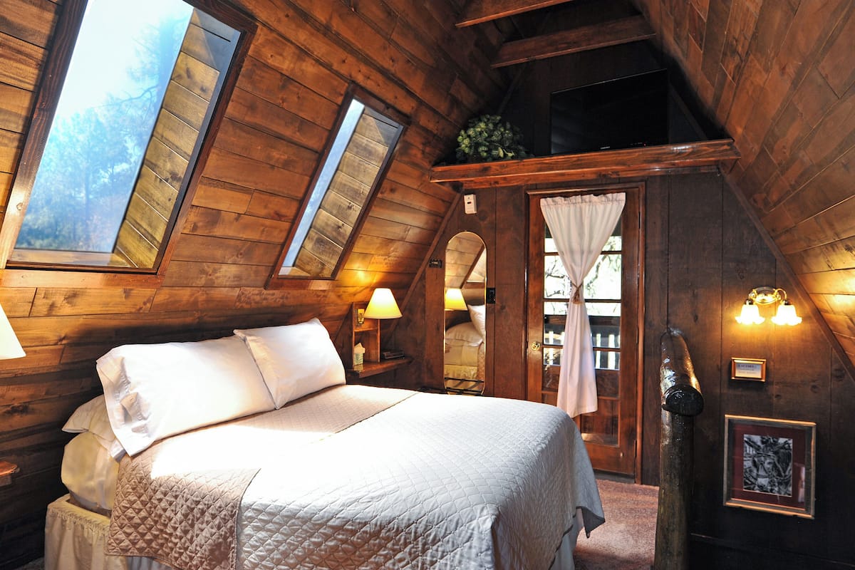 A cozy attic bedroom with a large bed, wooden walls, and a skylight.
