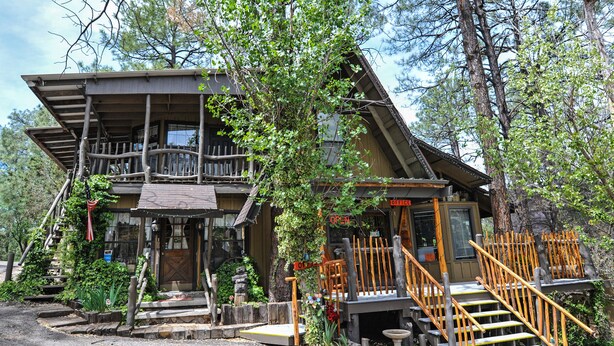 A rustic cabin with a wooden deck, a porch, and a staircase leading to the entrance. - Bear Creek Motel And Cabins (Silver City)