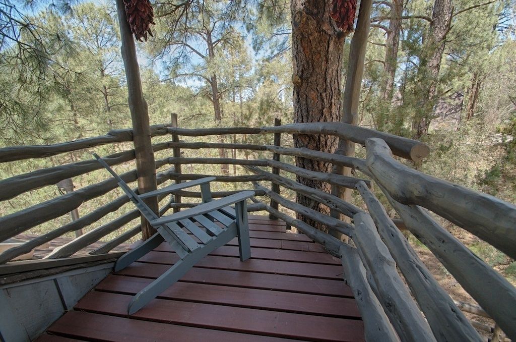 A wooden deck with a metal railing, surrounded by trees.