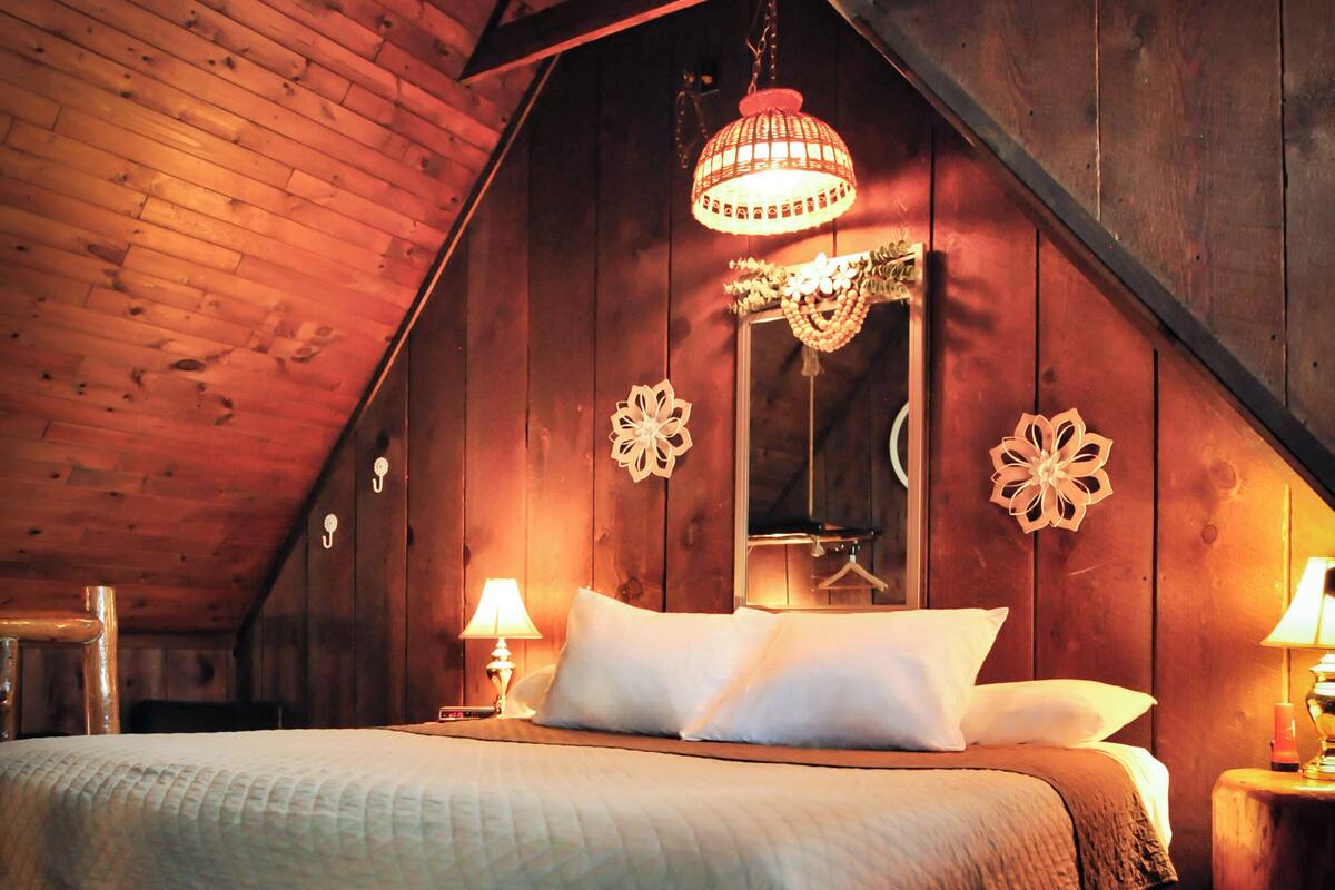 A cozy attic bedroom with a wooden ceiling, a large bed with white bedding, and two bedside lamps.