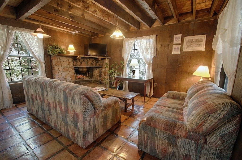 A cozy living room with a stone fireplace, two patterned sofas, a coffee table, and a television.