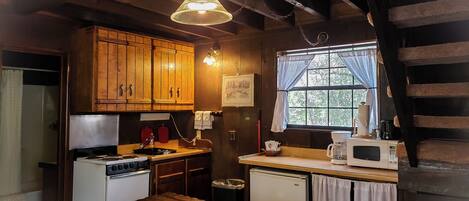 A rustic kitchen with wooden cabinets, a stove, a sink, and a window with curtains.