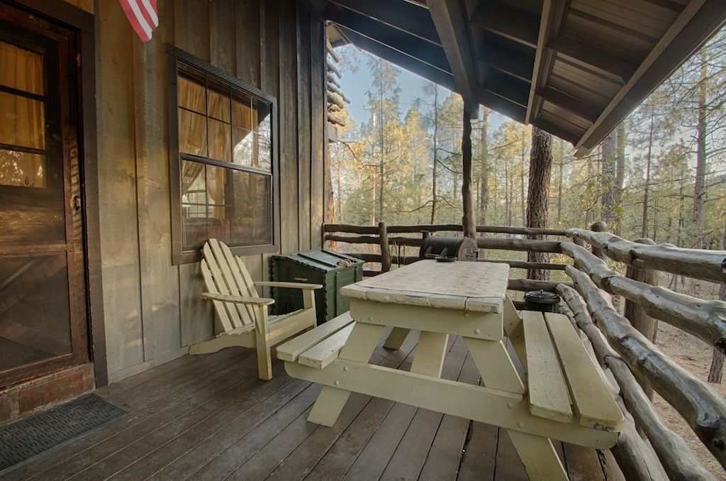 A wooden cabin with a porch, a picnic table, and a chair.