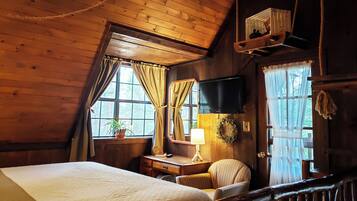 Une pièce confortable avec un lit, un bureau doté d’une lampe, une chaise, un téléviseur et une fenêtre avec des rideaux.