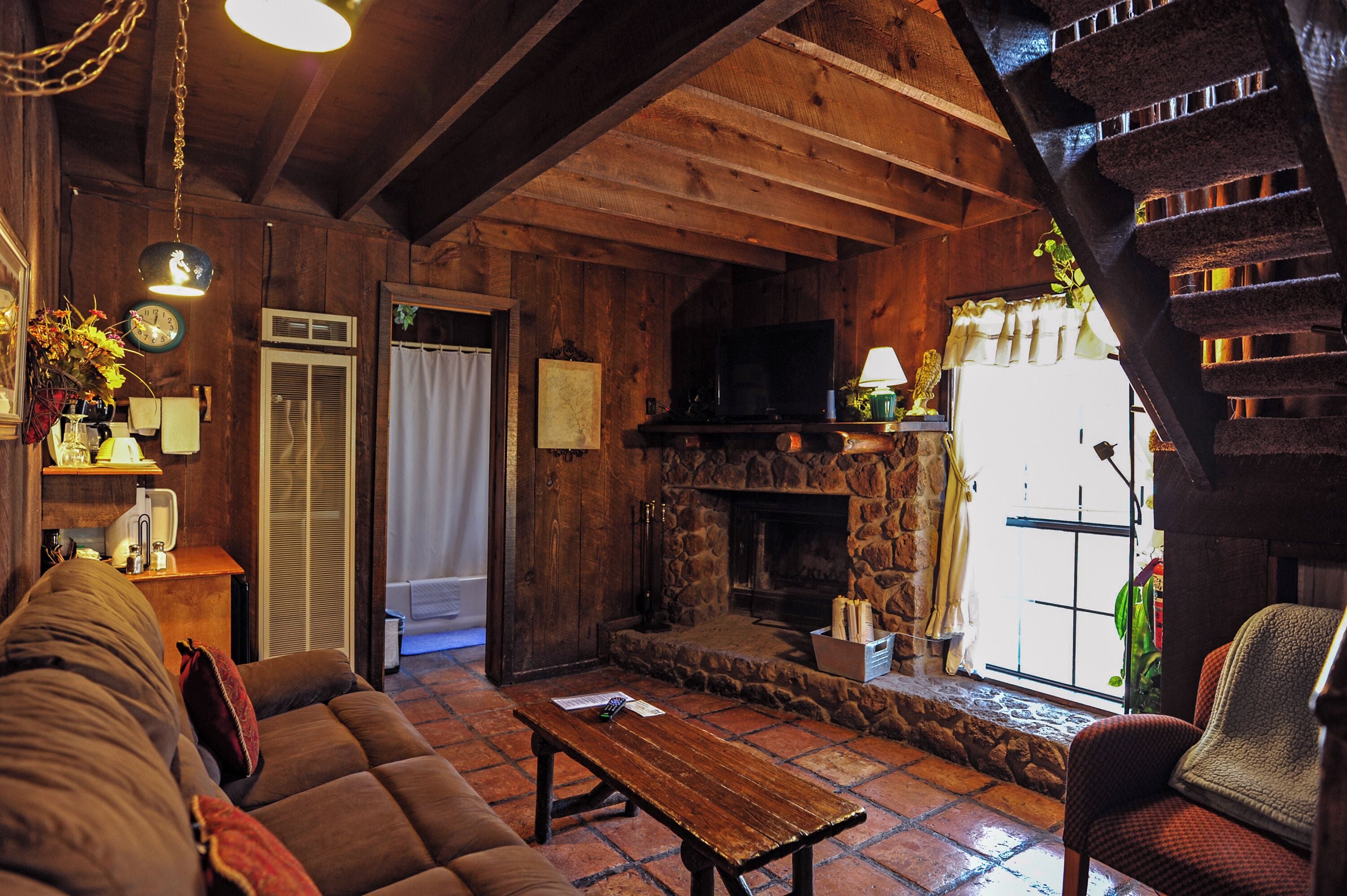 A cozy living room with a stone fireplace, wooden beams, a sofa, and a coffee table.
