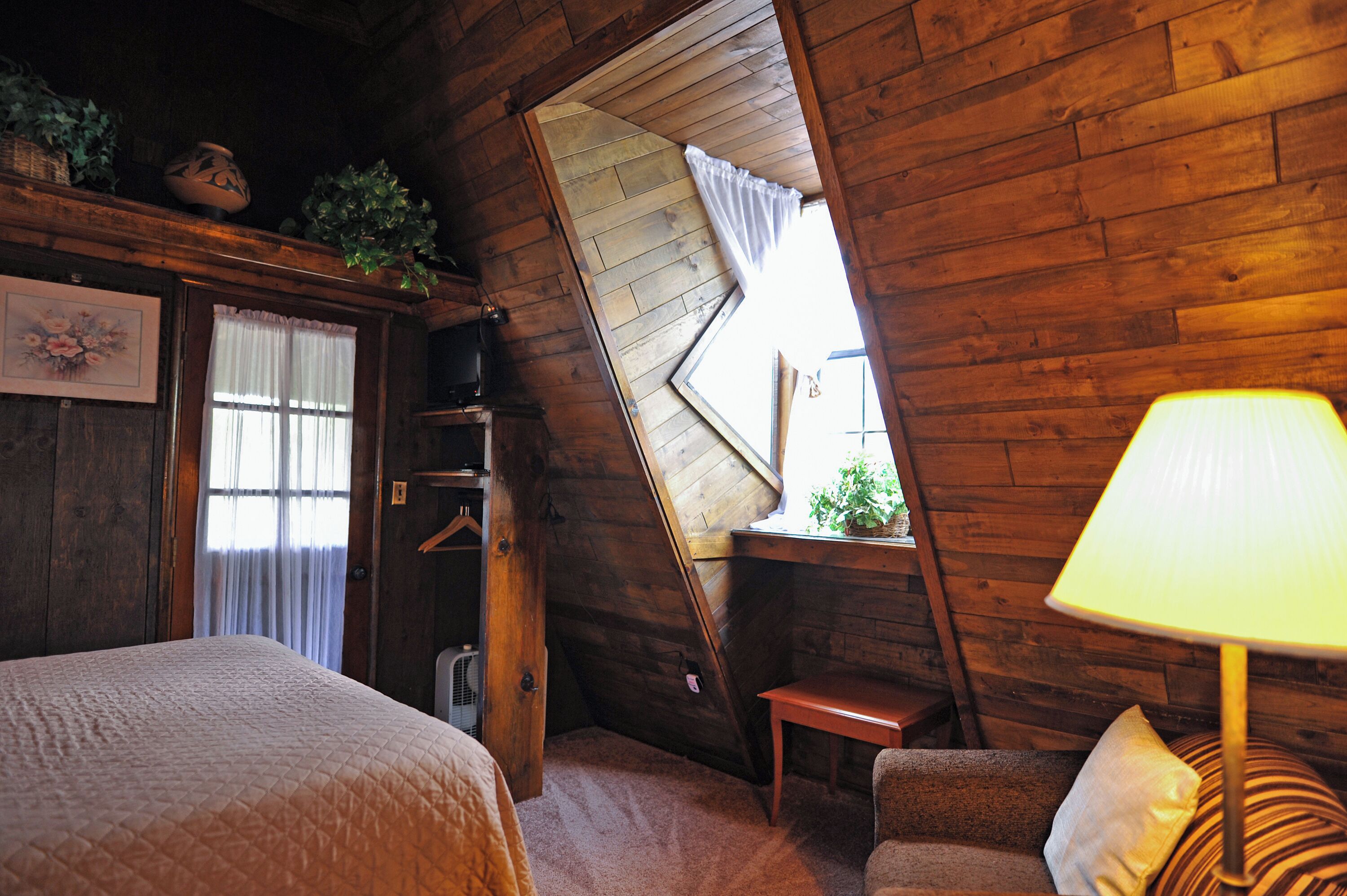 Ein gemütliches Schlafzimmer im Dachgeschoss mit schrägem Dach, einem Bett, einem Sessel, einem Tisch und einer Lampe.