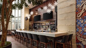 A bar area with a long counter, multiple bar stools, and a decorative wall with a floral pattern. - Archer Hotel Austin at the Domain (Austin)