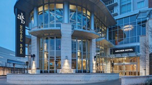 A modern hotel with a curved glass facade, a prominent bar area, and a well-lit entrance. - Archer Hotel Austin at the Domain (Austin)