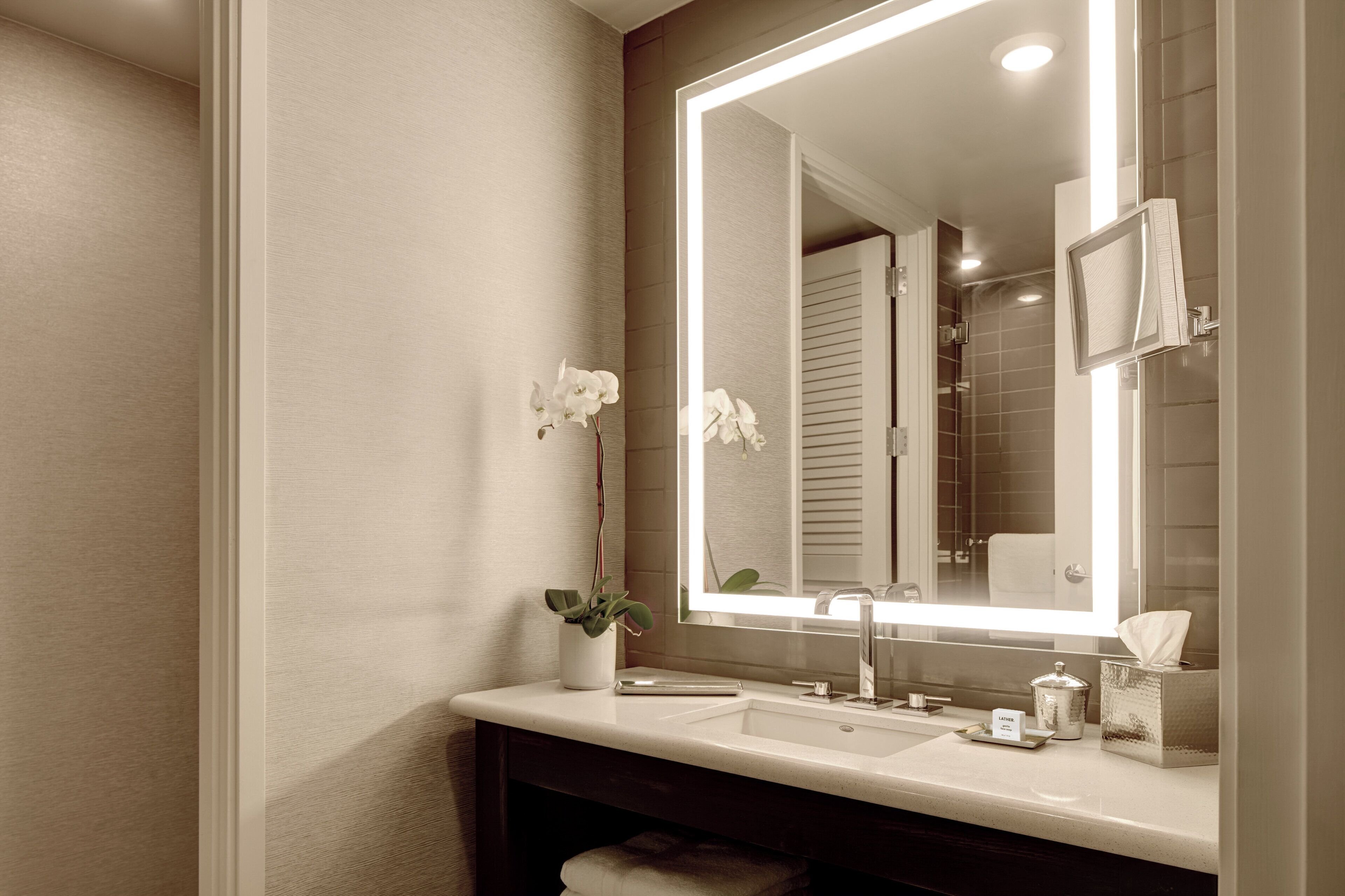 A bathroom with a large mirror, a sink, a towel, and a potted plant.