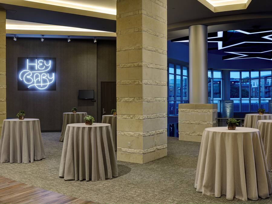 Um hall de hotel moderno com mesas redondas, um letreiro de neon com a frase
