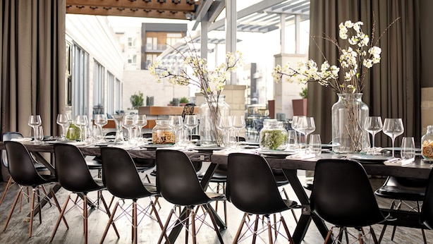 A dining area with a long table set for six, surrounded by black chairs with wooden legs. There are two vases with flowers on the table. - Archer Hotel Austin at the Domain (Austin)