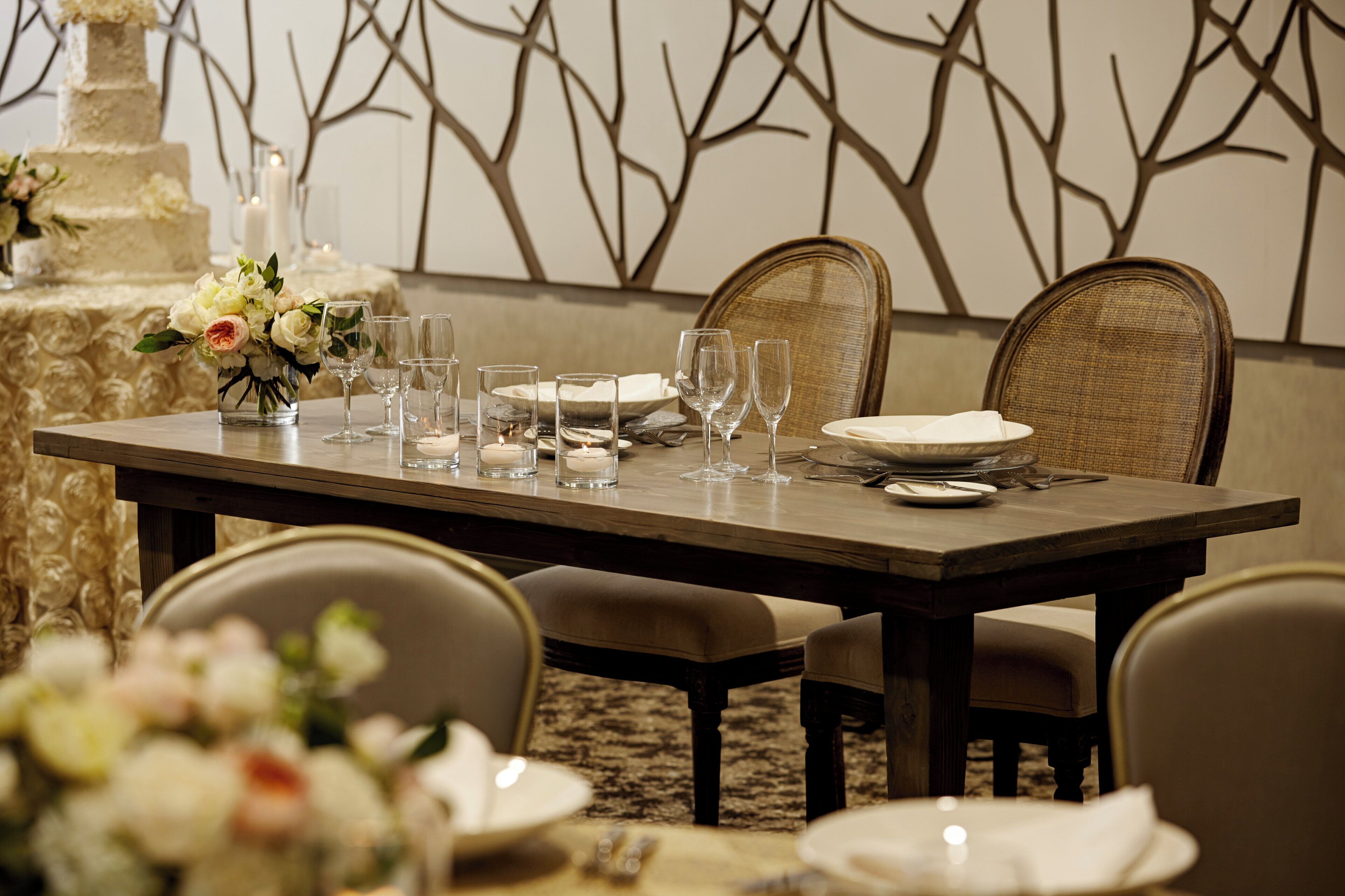 A dining table set with plates, glasses, and a vase of flowers.