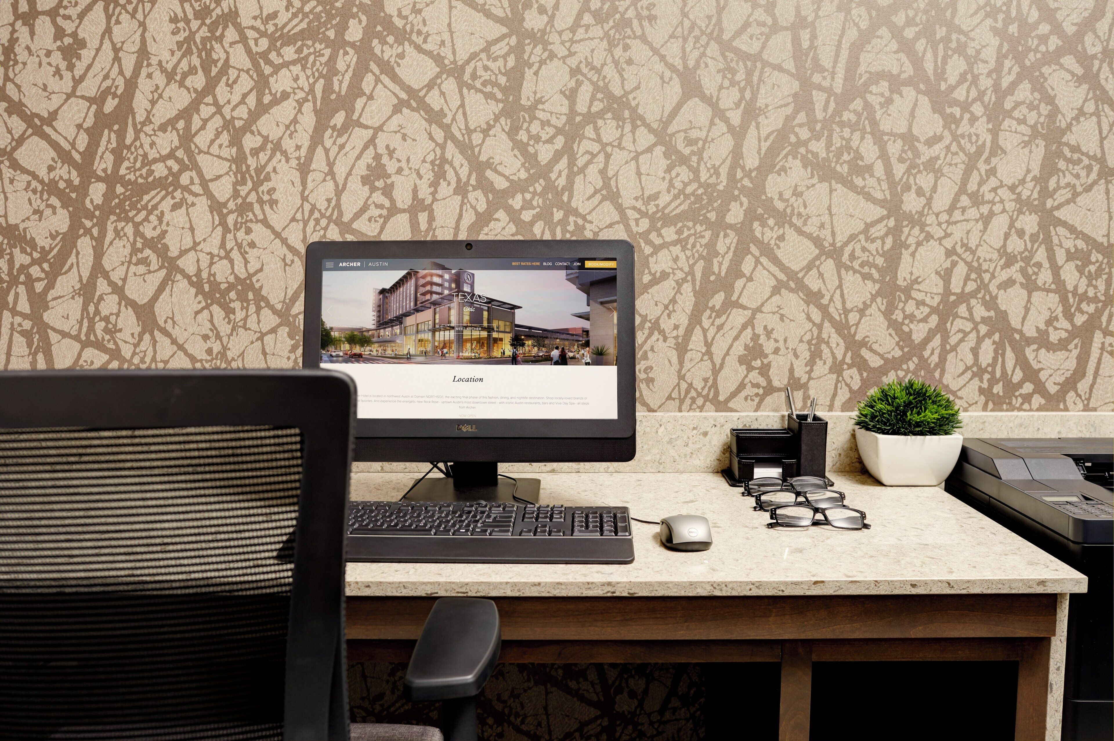 A computer desk with a monitor displaying a building image, a keyboard, a mouse, a plant, and a printer.