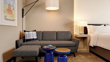 Une chambre d’hôtel avec un canapé, deux poufs bleus, une table de chevet avec une lampe et un lit.