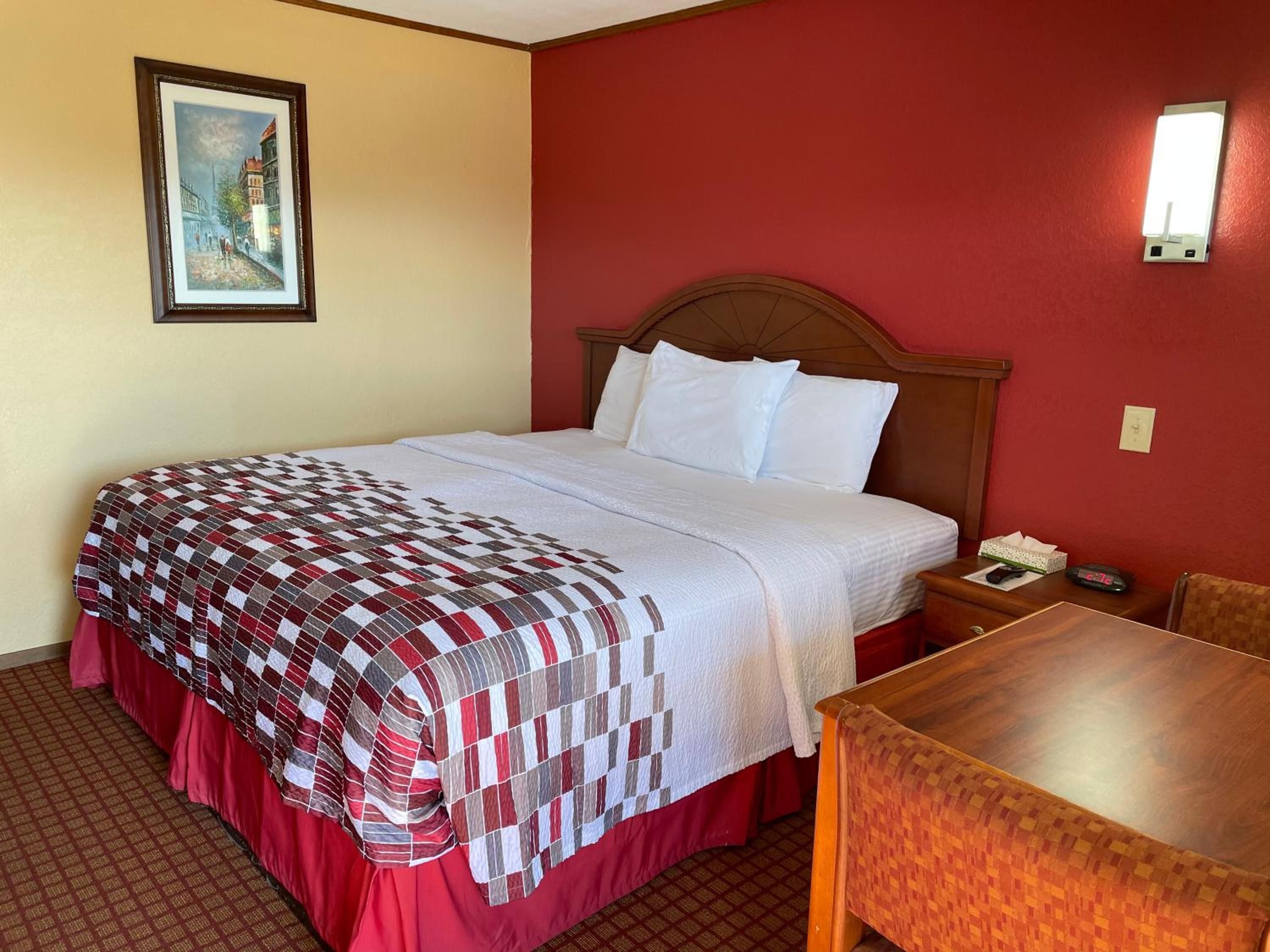 Ein Hotelzimmer mit Bett, Nachttisch, Tisch und einem Gemälde an der Wand.