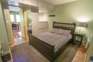Un dormitorio con cama, mesita de noche y lámpara. Hay un escritorio y una silla en la habitación contigua.