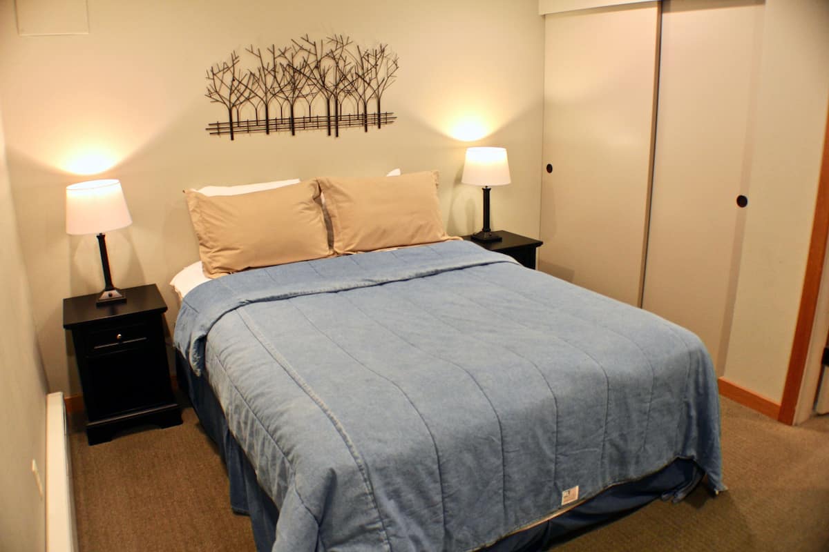 A bedroom with a bed, two bedside tables, and a wall-mounted artwork.