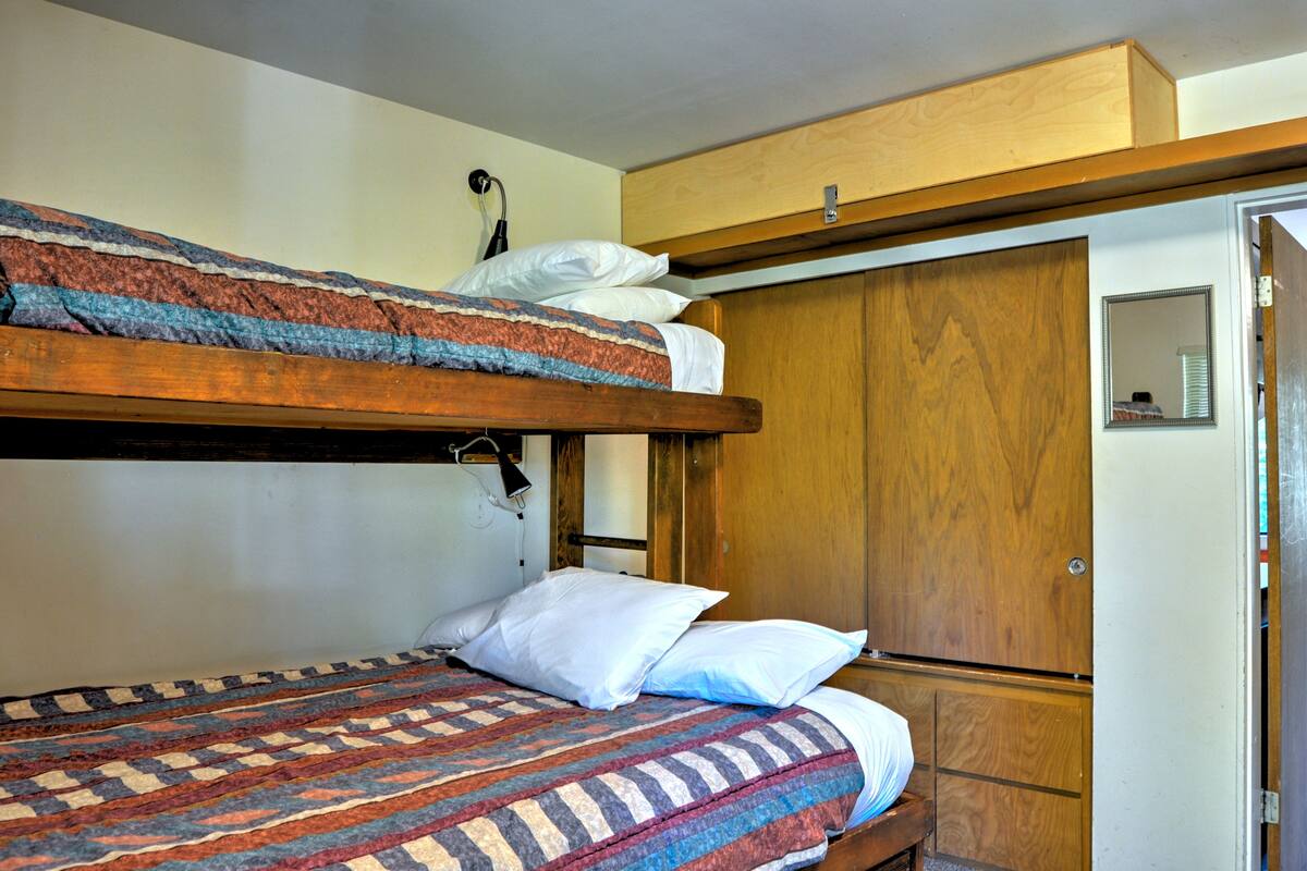 A bunk bed with a patterned blanket, a wooden wardrobe, and a mirror on the wall.