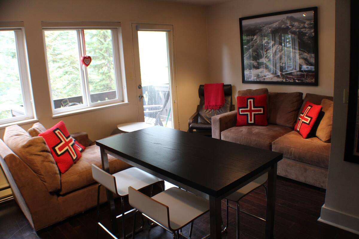 A living room with a dark wooden table, two sofas with red pillows, and a framed picture on the wall.