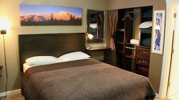A hotel room with a large bed, a wardrobe, a mirror, and a painting of mountains.